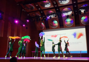 Studentki tańczą na scenie z kolorowymi chustami